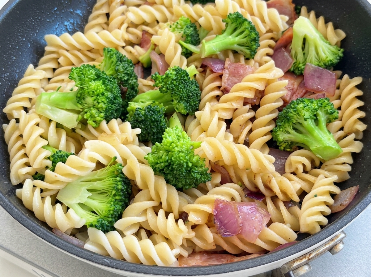 Black pepper being seasoned over the stir-fried pasta and broccoli while being tossed with a spatula.