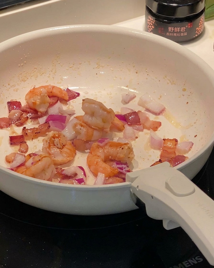 Slices of button mushrooms being tossed with the bacon, shrimp, and onion mixture.