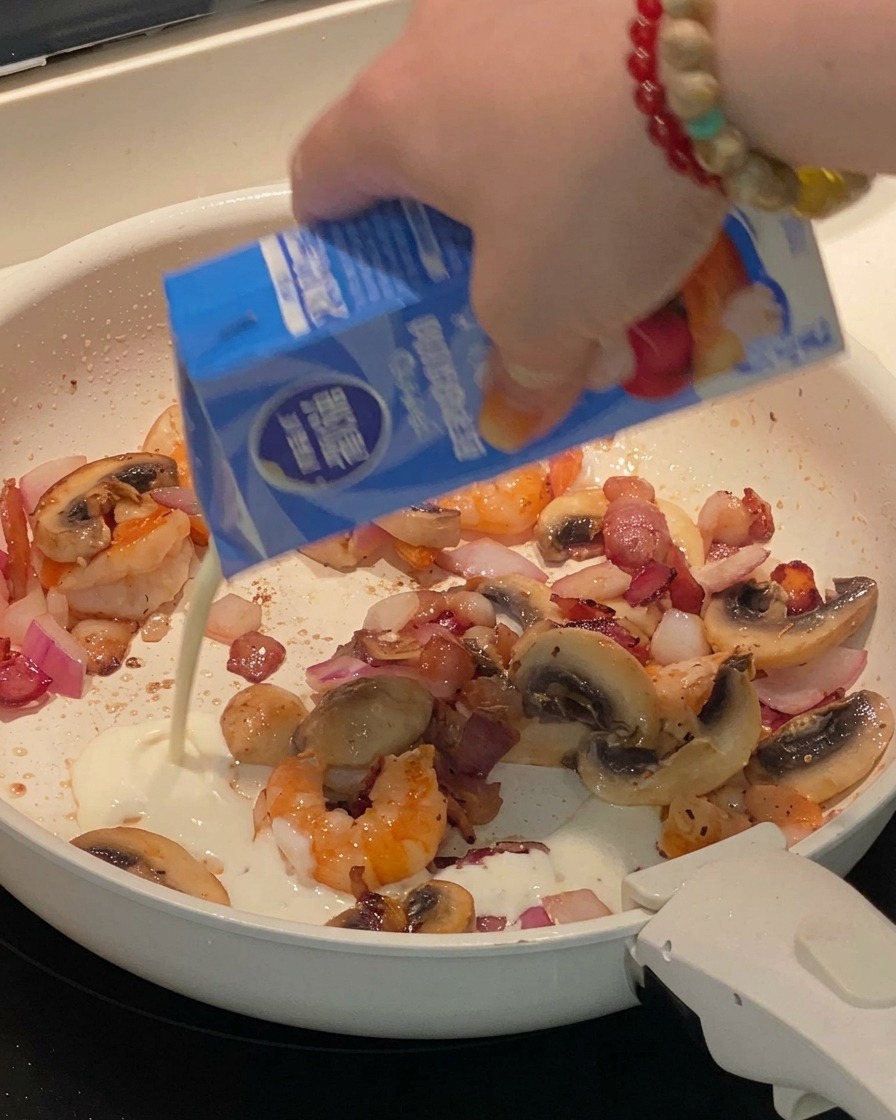 Heavy cream and milk being poured into the pan, swirling with the cooked ingredients.