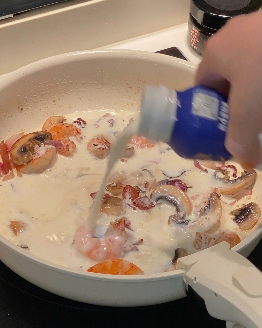 Cooked tube pasta being tossed in a creamy sauce with shrimp and mushrooms in a pan.