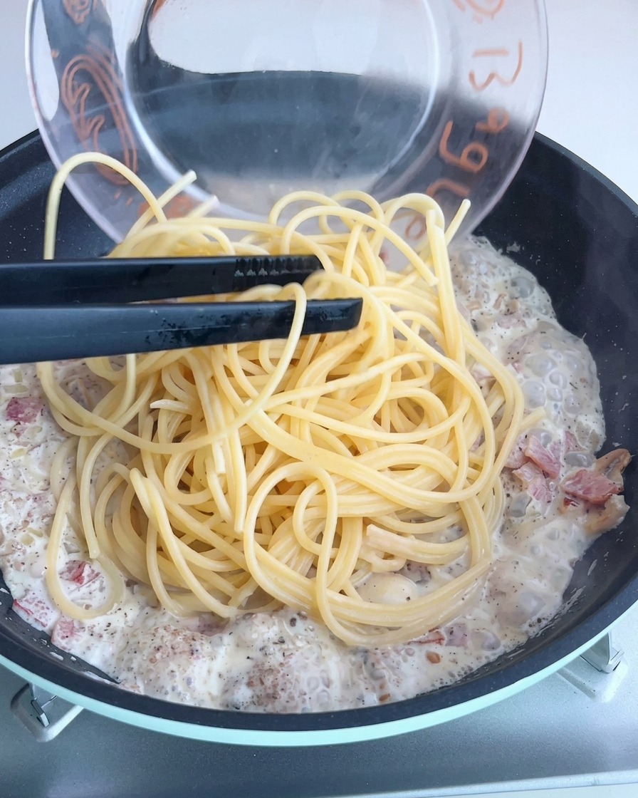Spaghetti noodles being tossed in a creamy truffle sauce in a pan.