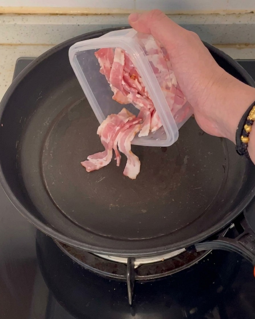 Chopped raw bacon pieces being added to a clean, empty non-stick frying pan.