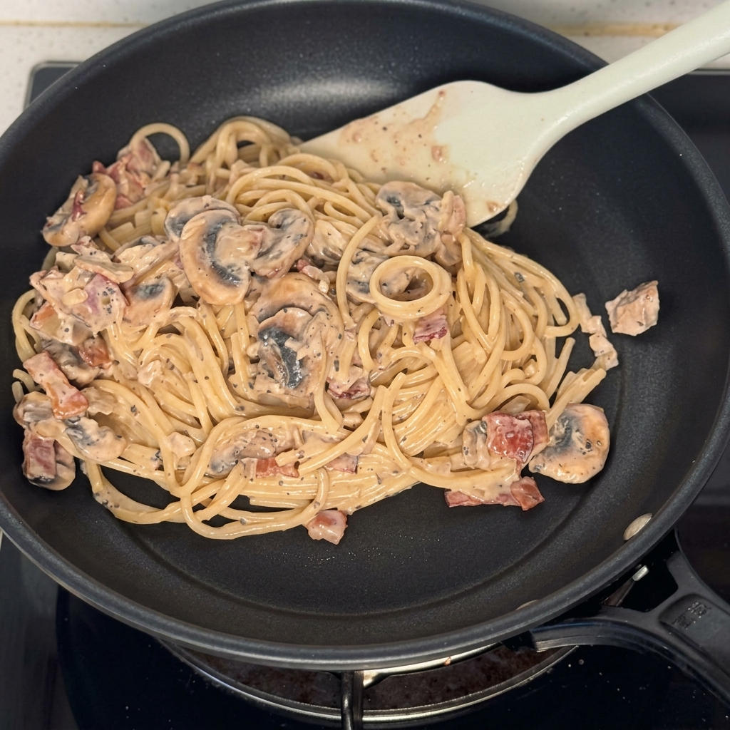 A pan filled with coated spaghetti mushrooms and bacon pieces