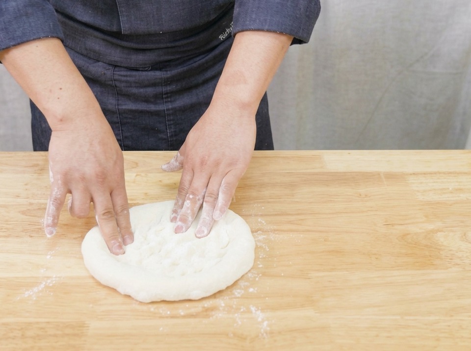 A close-up view of hands gently stretching and shaping a round pizza dough on a wooden board.