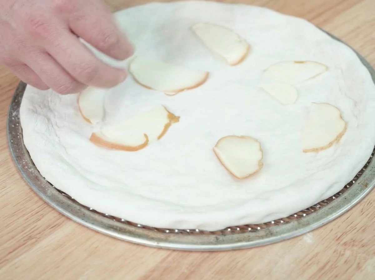 Slices of smoked cheese being arranged on top of a raw pizza dough base.