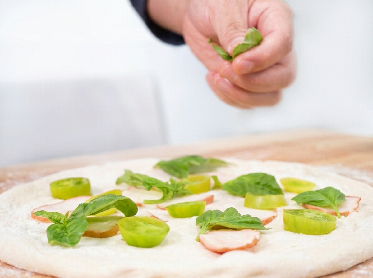 Fresh basil leaves being sprinkled over the pizza ingredients.