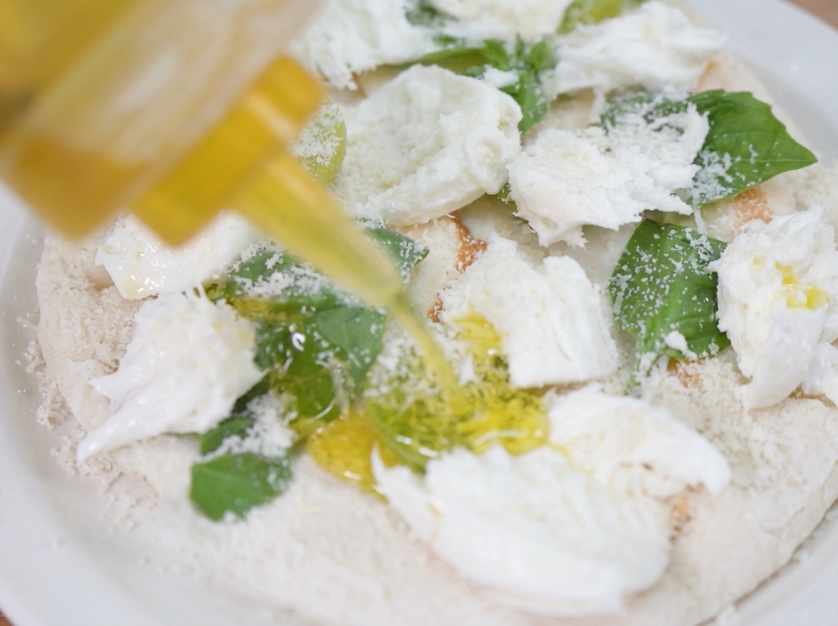 A thin stream of olive oil being drizzled over the assembled pizza.
