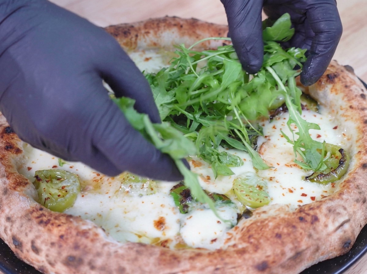 Fresh green arugula leaves being placed on top of a baked, bubbling pizza.