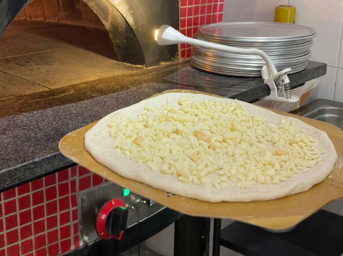 A pizza being transferred into a high-temperature stone oven with a wooden peel.