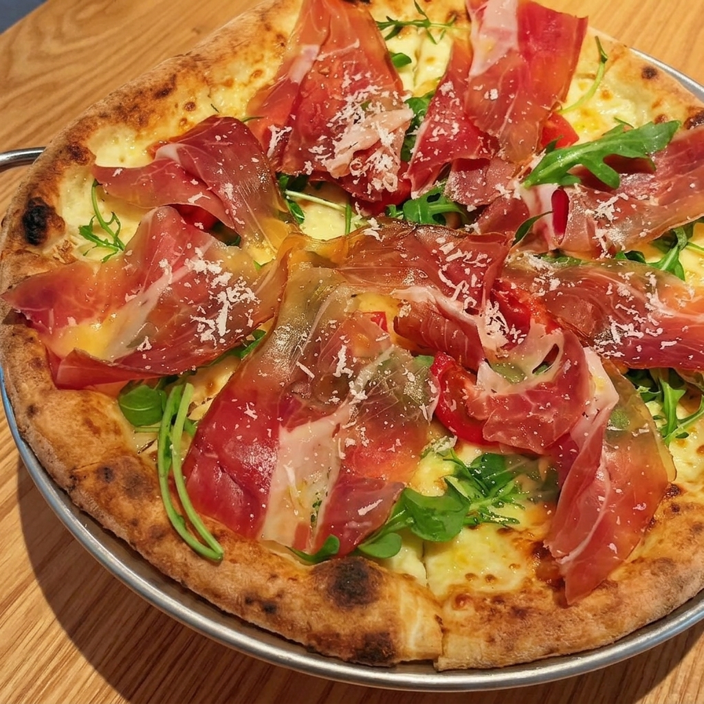 Thin, delicate ribbons of raw Parma ham layered on top of fresh arugula and cherry tomatoes on a cooked pizza base.