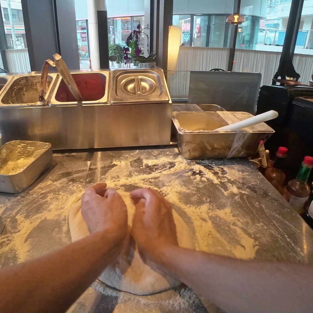 Pizza dough being gently pressed and flattened into a round shape on a floured wooden surface.