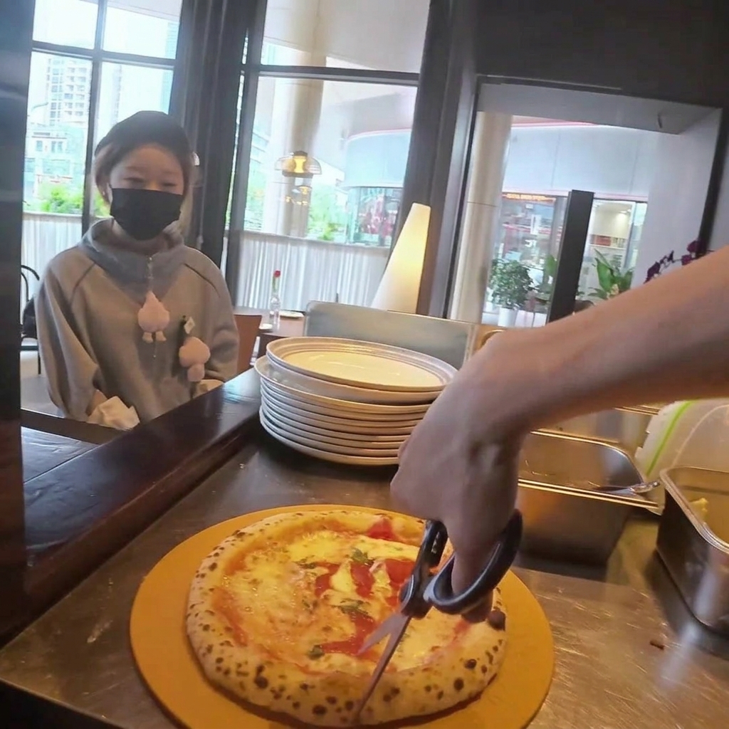 A pizza being cut into wedges using a circular pizza cutter on a wooden cutting board.