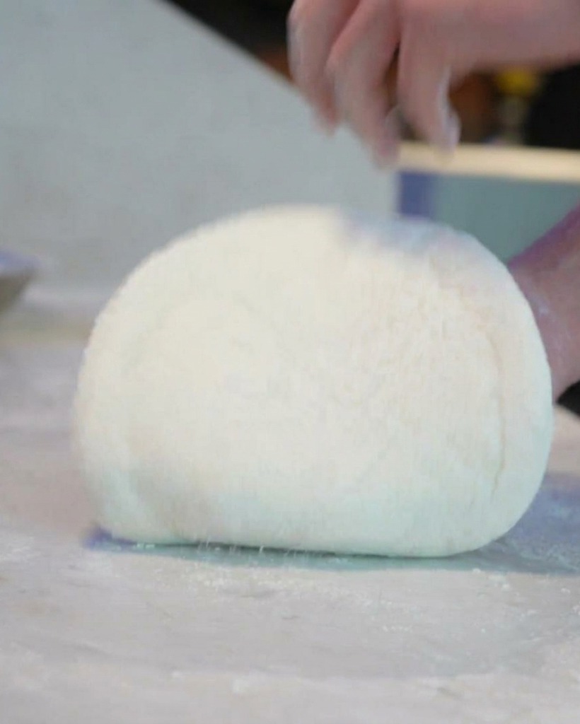 The chef stretching and rotating a raw circle of pizza dough.