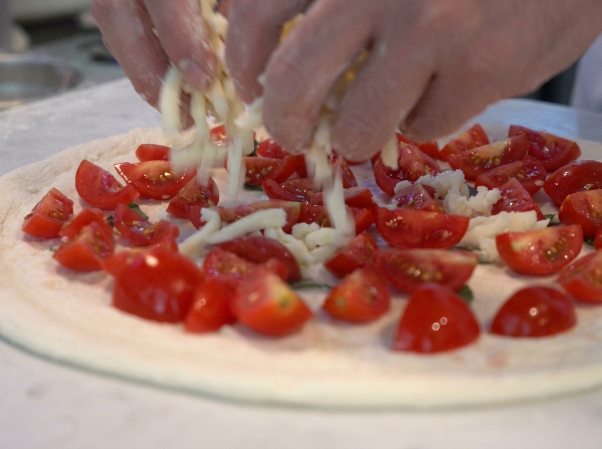 Chunks of mozzarella being added to a pizza topped with fresh chopped tomatoes and basil.