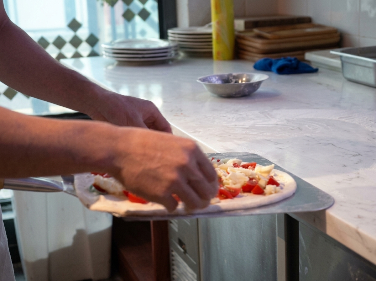 A chef holding a raw pizza on a metal peel, gently adjusting and stretching the dough edges before baking.