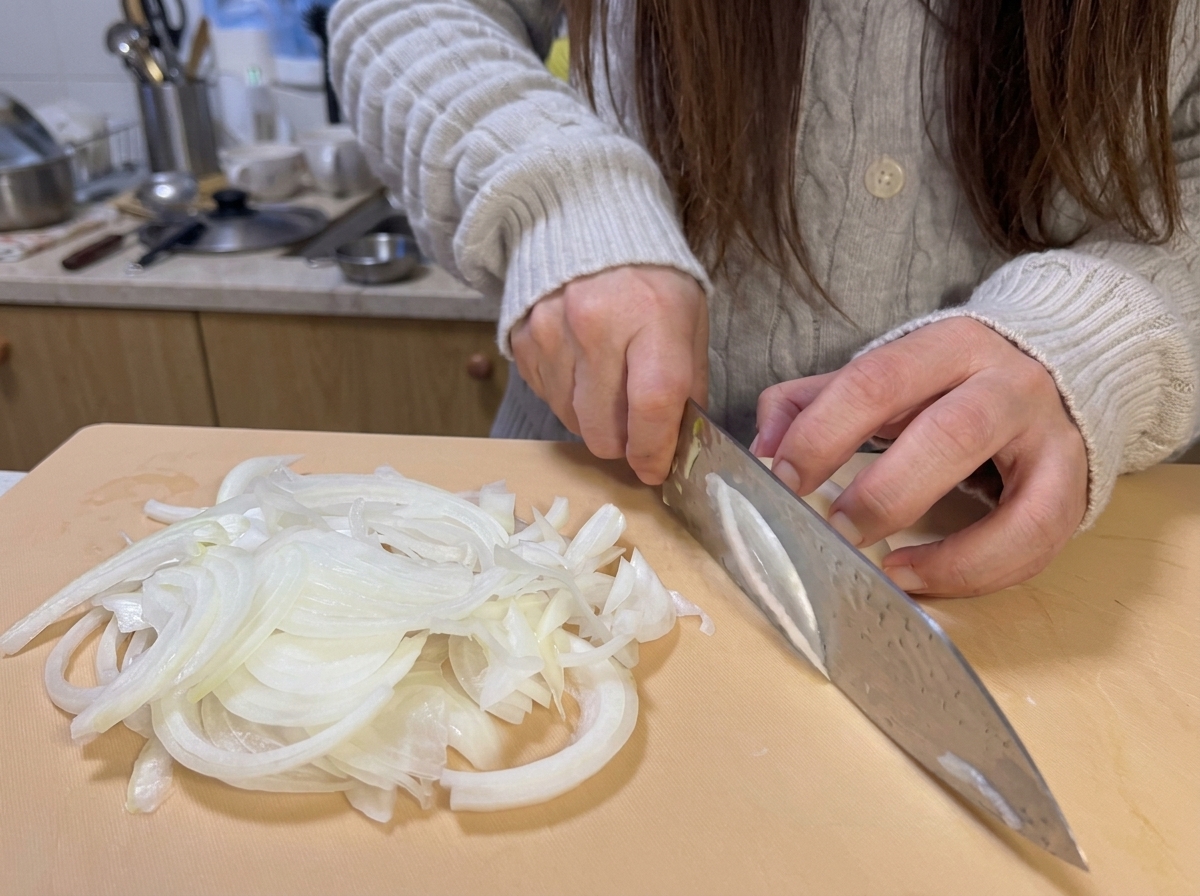 Fresh onion slices thinly cut on a light-colored cutting board, ready for cooking.