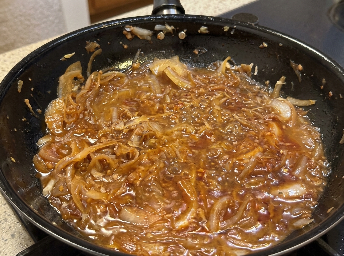 Parmesan cheese being grated into a pan with creamy onion sauce as cream is poured in.