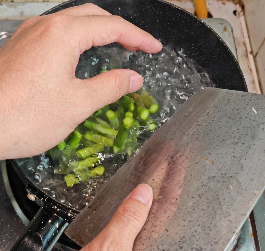 Green asparagus sections being removed from a pot of boiling water with a slotted spoon.