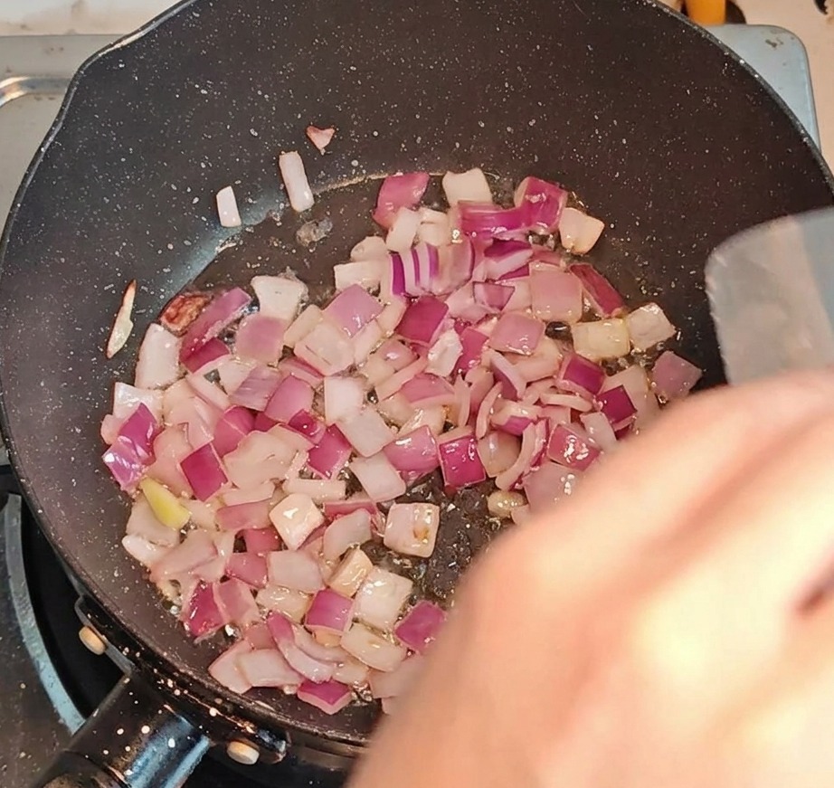 Diced bacon and onions frying together in a pan over high heat.