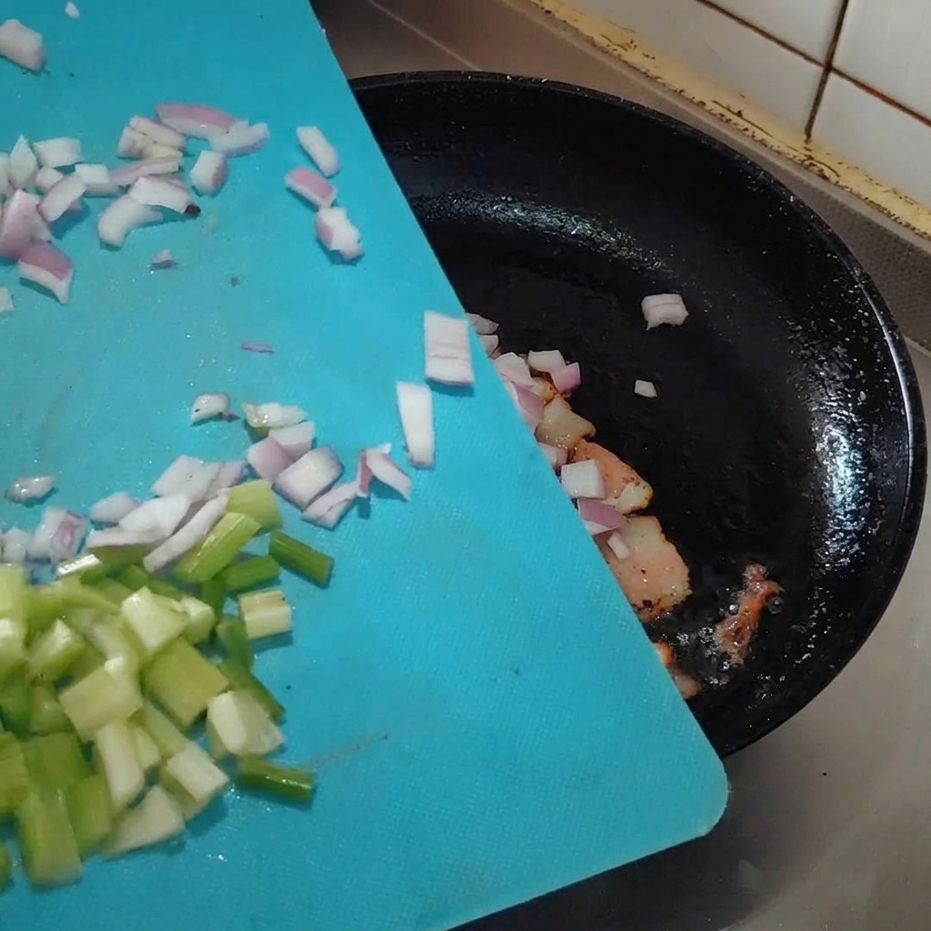 Minced aromatics being added to the pan with frying bacon.