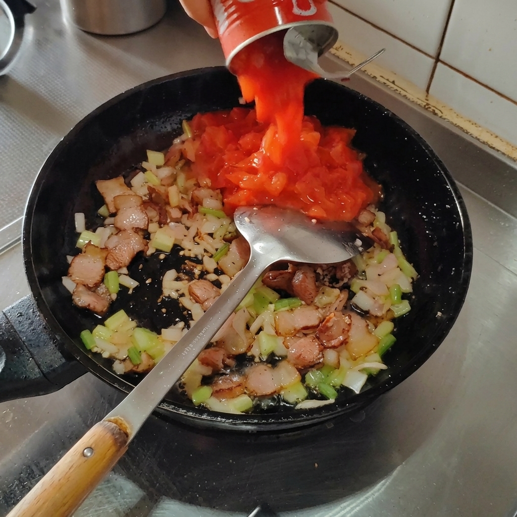 Canned tomatoes being poured into the pan over the bacon and aromatics mixture.
