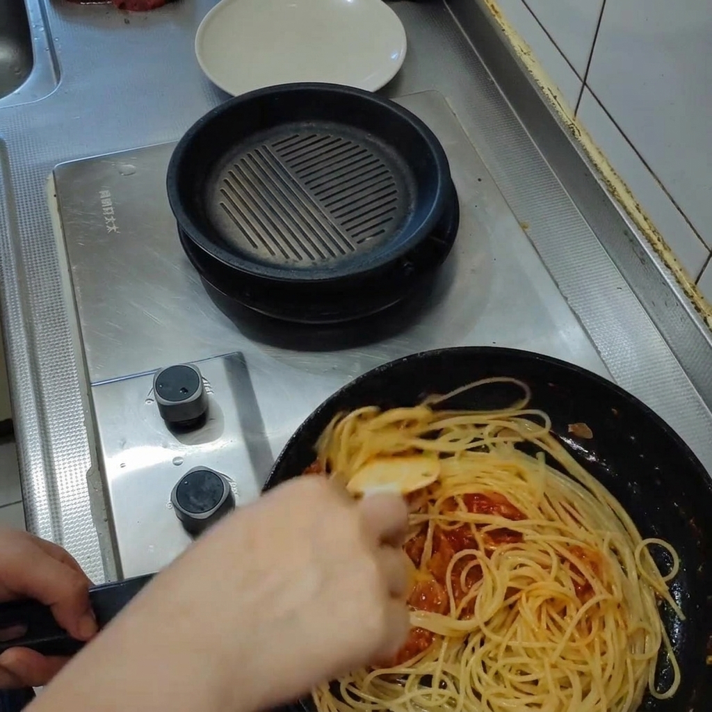 Pasta tossing in a rich tomato sauce inside a frying pan, with steam rising as the sauce emulsifies.