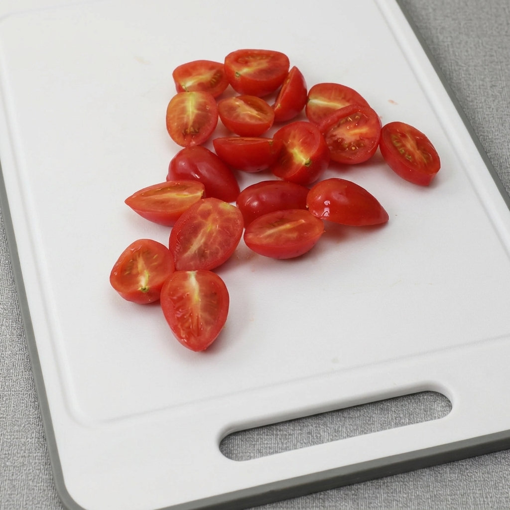 Cherry tomatoes sliced in half, arranged on a white cutting board.