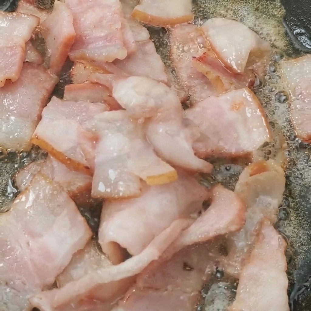 Halved cherry tomatoes in a pan, cooking alongside crispy bacon pieces.