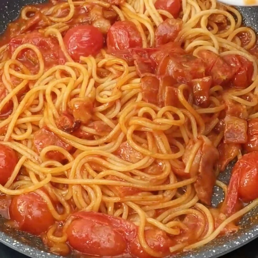 A pan of saucy spaghetti being topped with a layer of finely grated cheese.