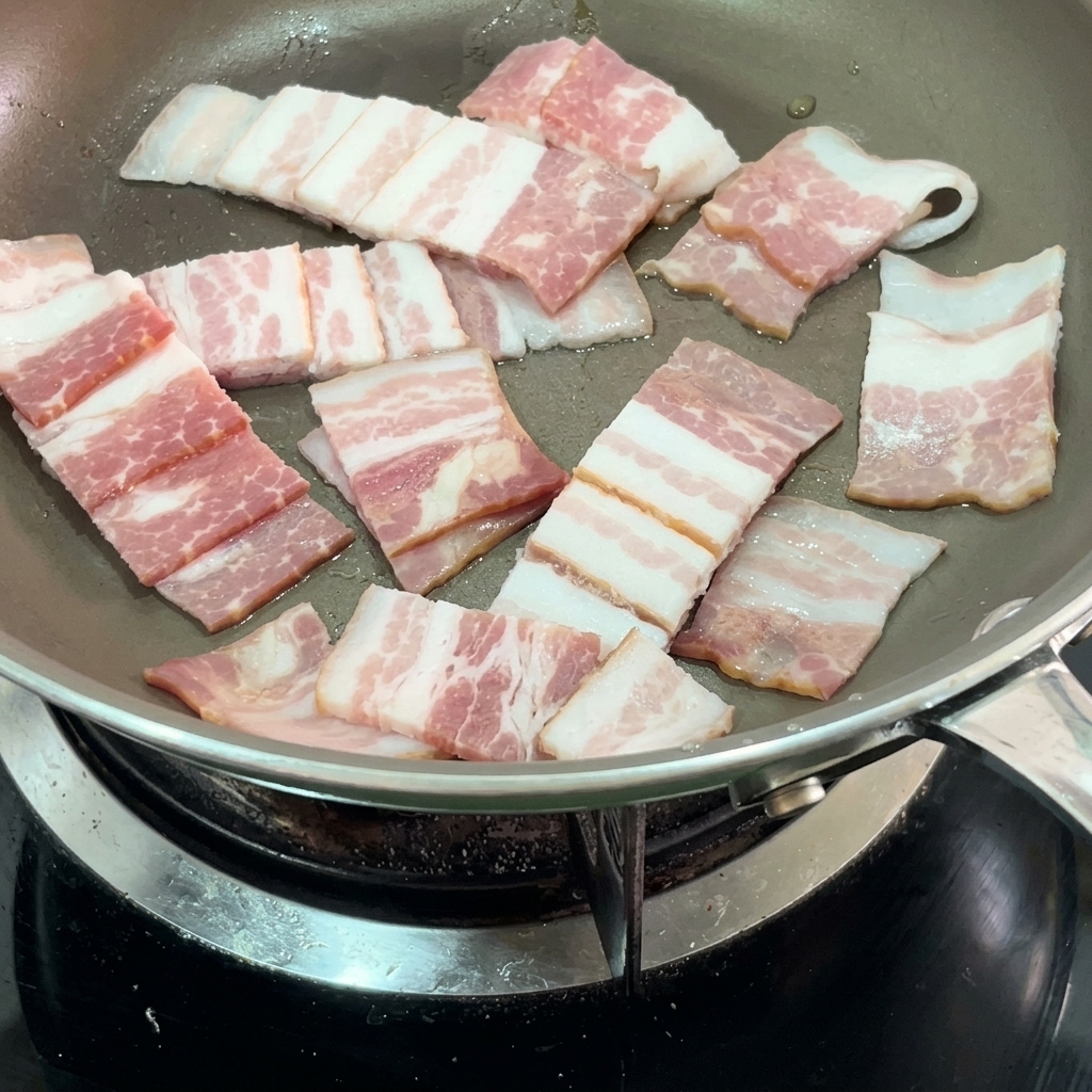 Crispy bacon strips frying in a pan.