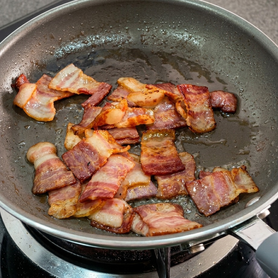 Rendered bacon fat and golden brown bacon pieces in a frying pan.