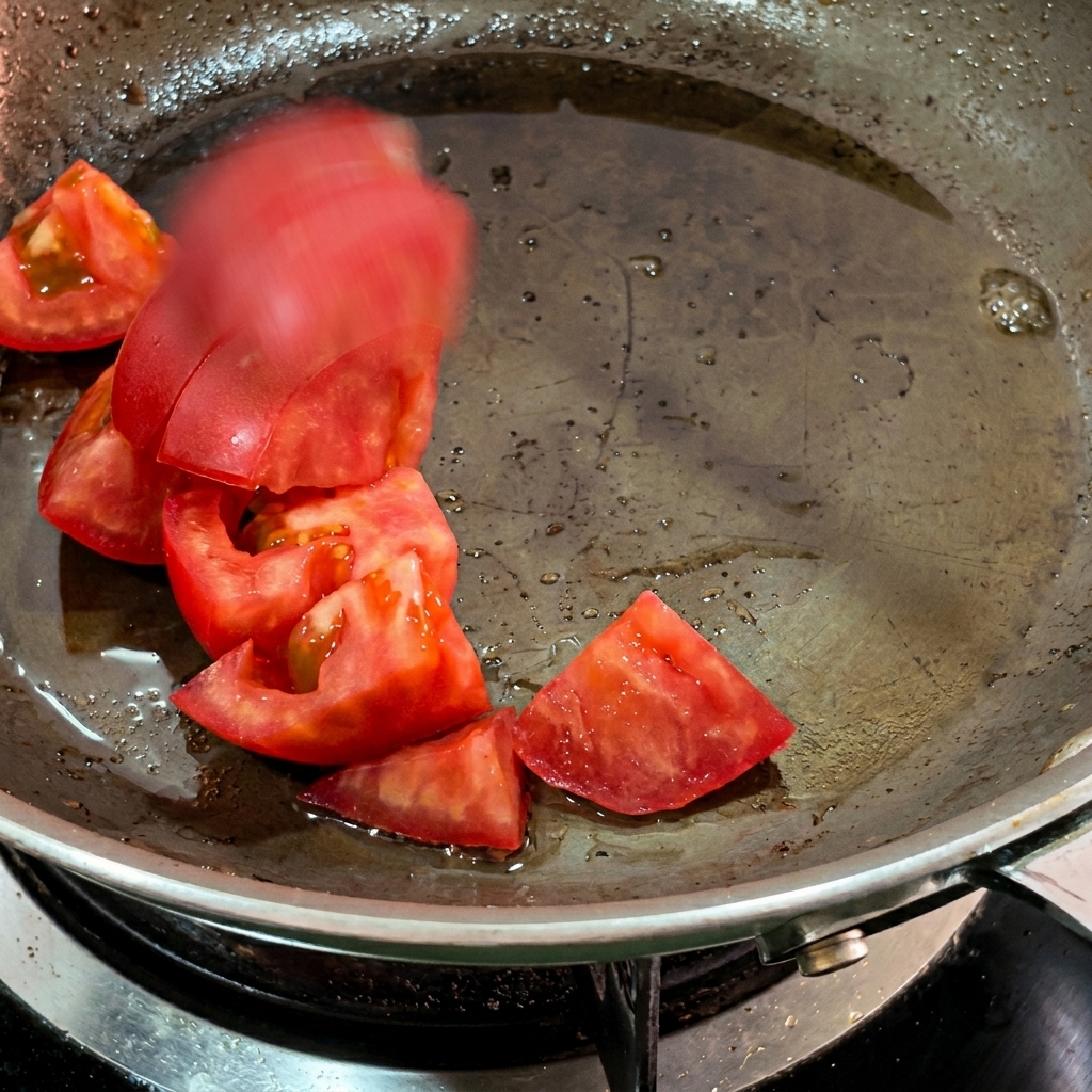 Tomato chunks softening in rendered bacon fat in a pan.