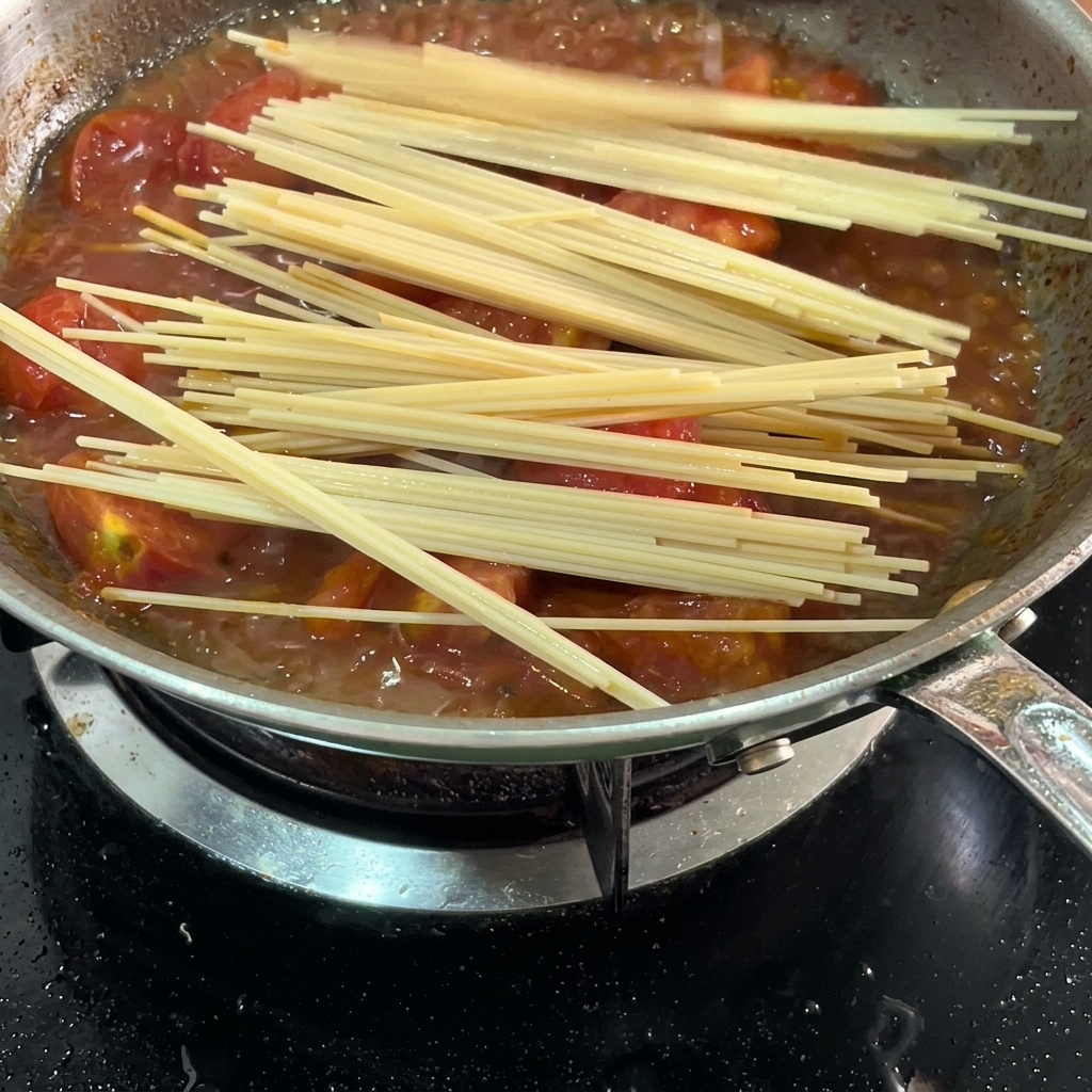 Long spaghetti noodles soaking in the tomato sauce in the pan.