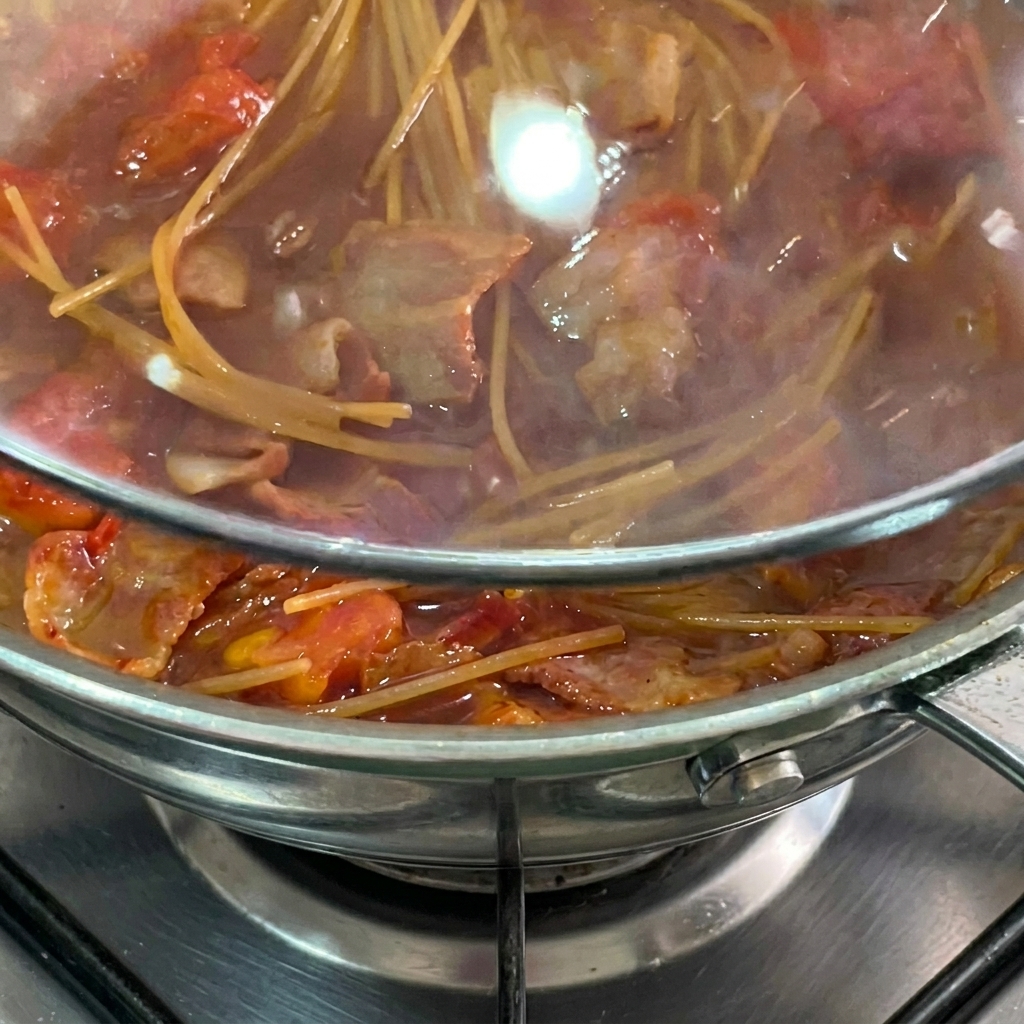 Spaghetti simmering in tomato sauce under a glass lid.