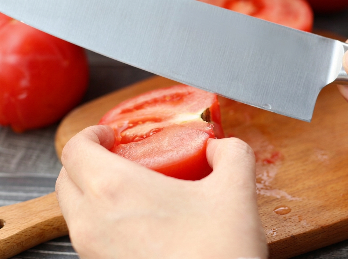 A knife slicing through a peeled tomato on a wooden cutting board.