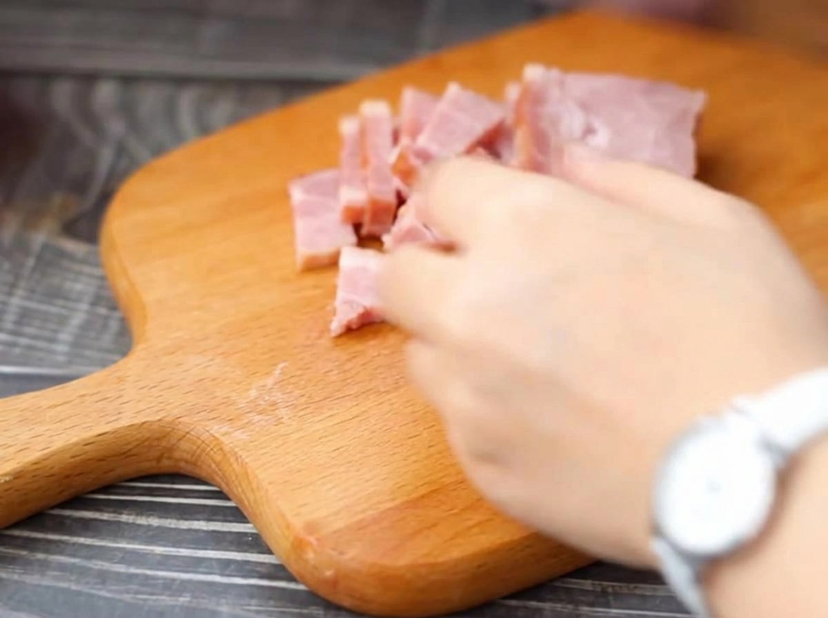 Strips of bacon being cut into smaller pieces on a wooden cutting board.