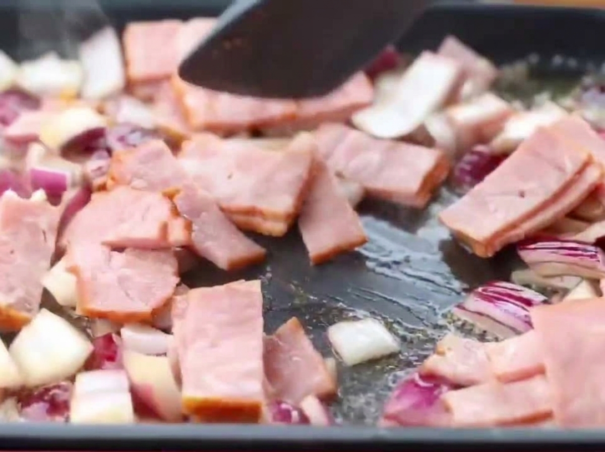 Bacon slices and diced red onions frying together in a pan.