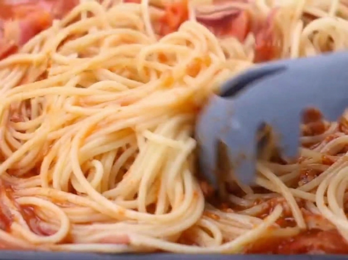 Cooked spaghetti being added to the tomato and bacon sauce.