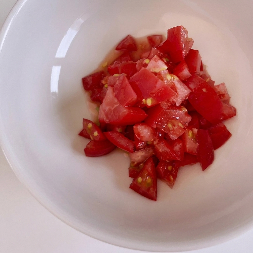 Fresh red tomatoes being chopped into small cubes on a wooden cutting board.