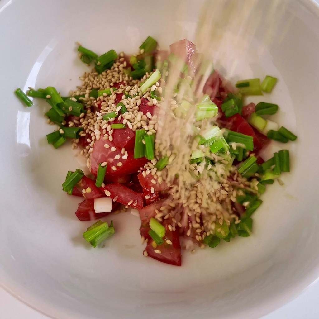 A bowl containing diced red tomatoes, chopped green onions, and sesame seeds.