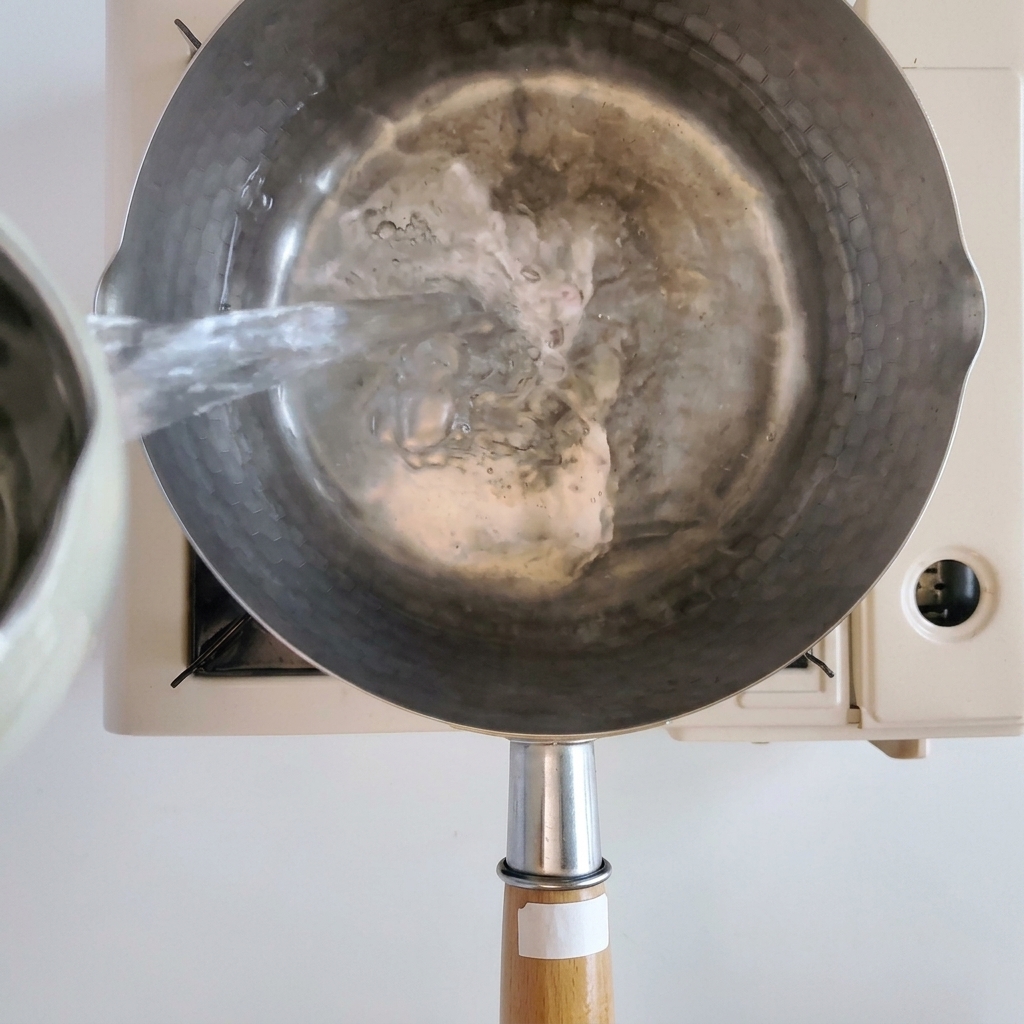 Enoki mushrooms and udon noodles cooking in a pot of boiling water.