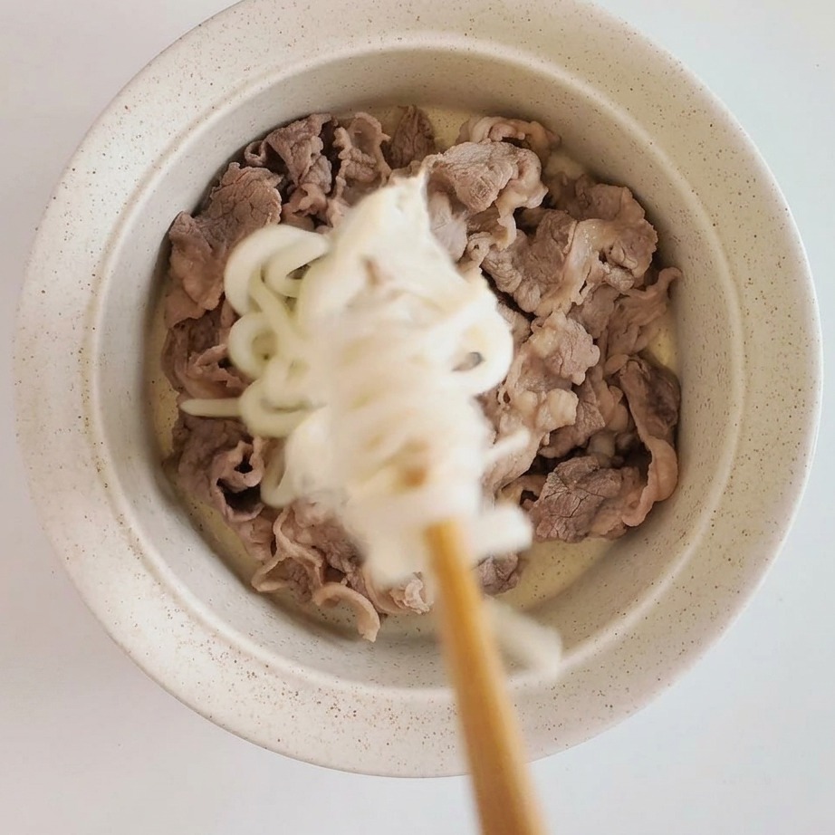 Assembled bowl featuring tender blanched beef slices topped with chilled udon noodles and enoki mushrooms.
