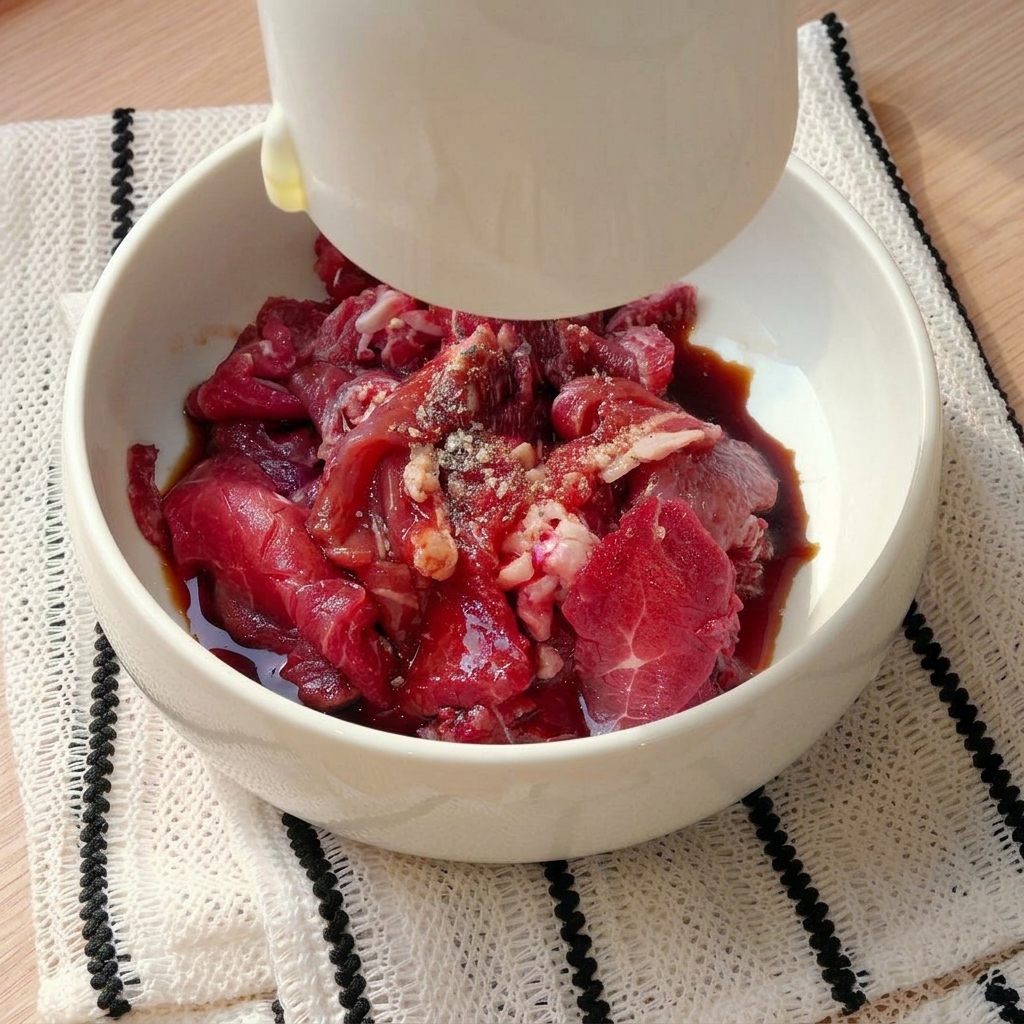 Raw beef slices in a white bowl being seasoned with liquid ingredients and spices from a small white cup.