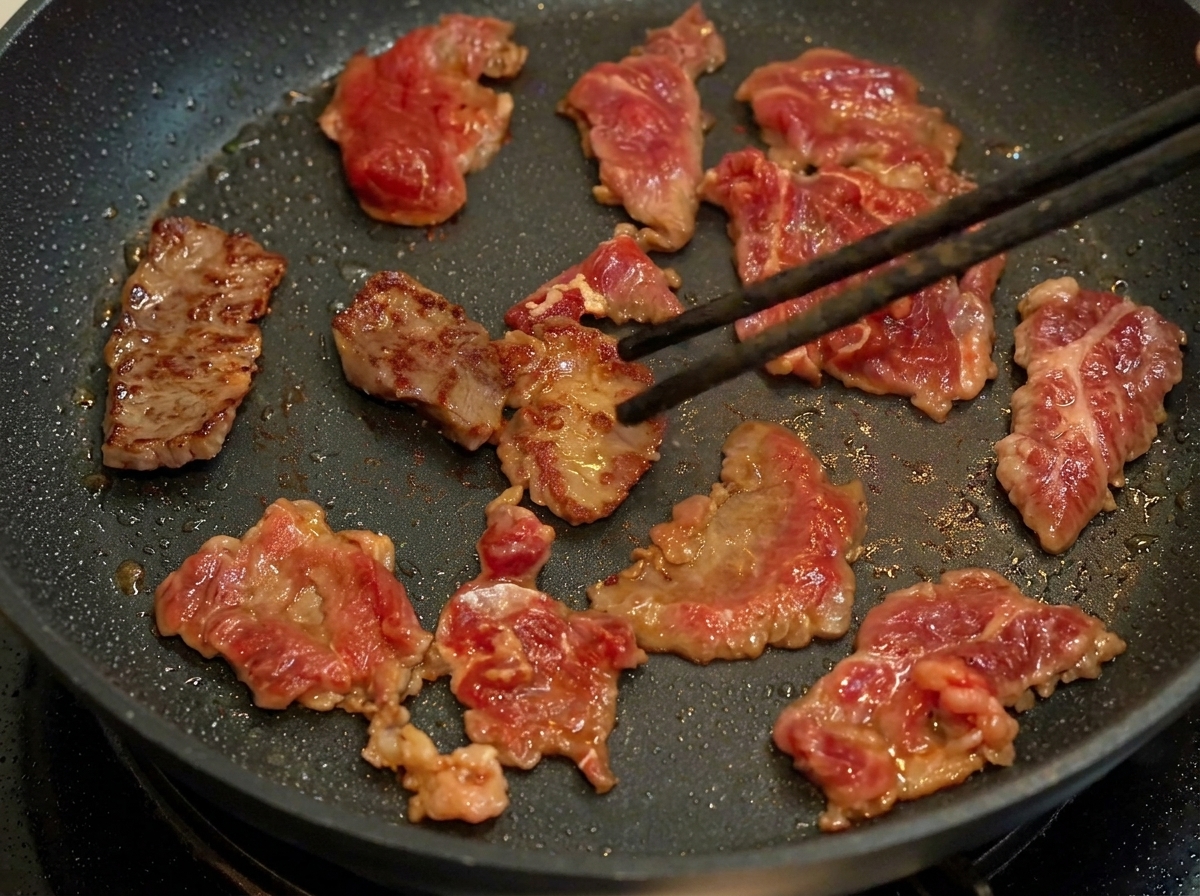 Slices of marinated beef browning in a hot skillet.