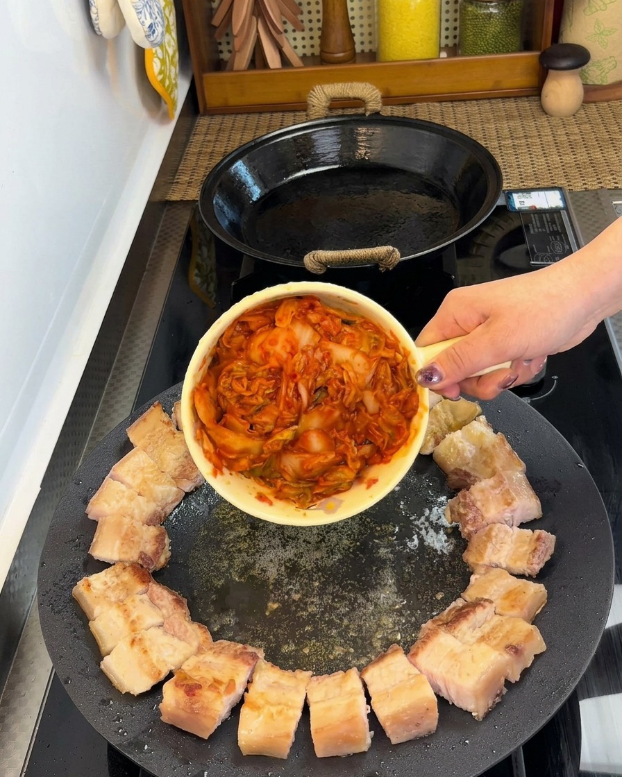 Pork belly pieces neatly arranged in a circle with a portion of kimchi placed in the center of the pan.