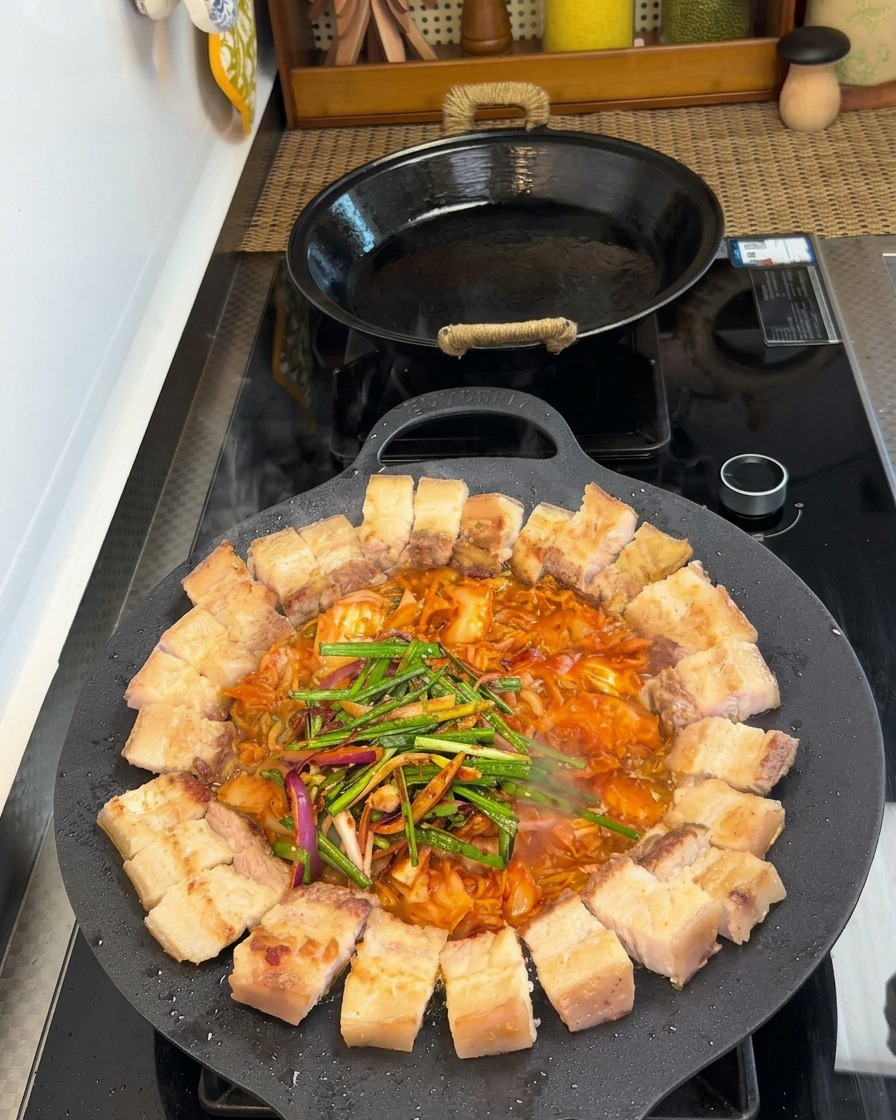 Pork belly and kimchi in a pan topped with fresh leeks, onions, and various seasonings.