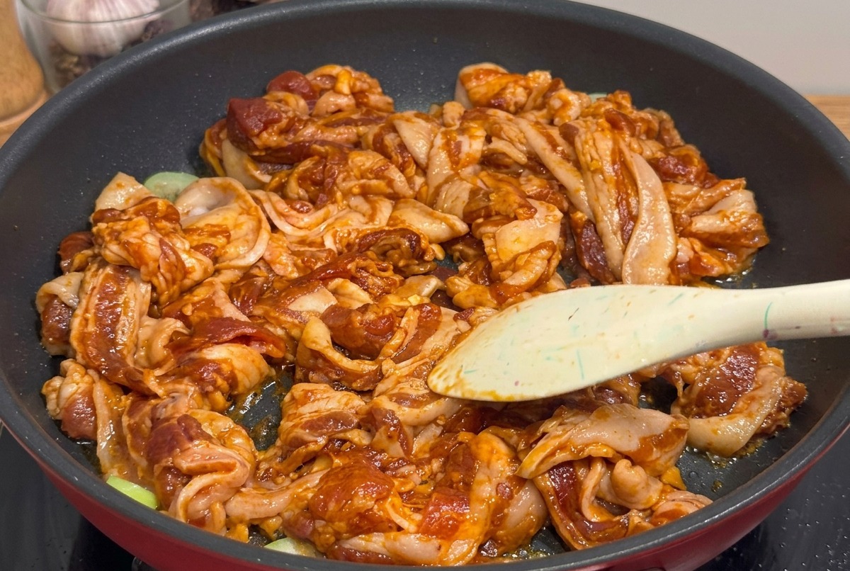 Bite-sized pieces of grilled, glazed pork belly being cut with shears in a pan.