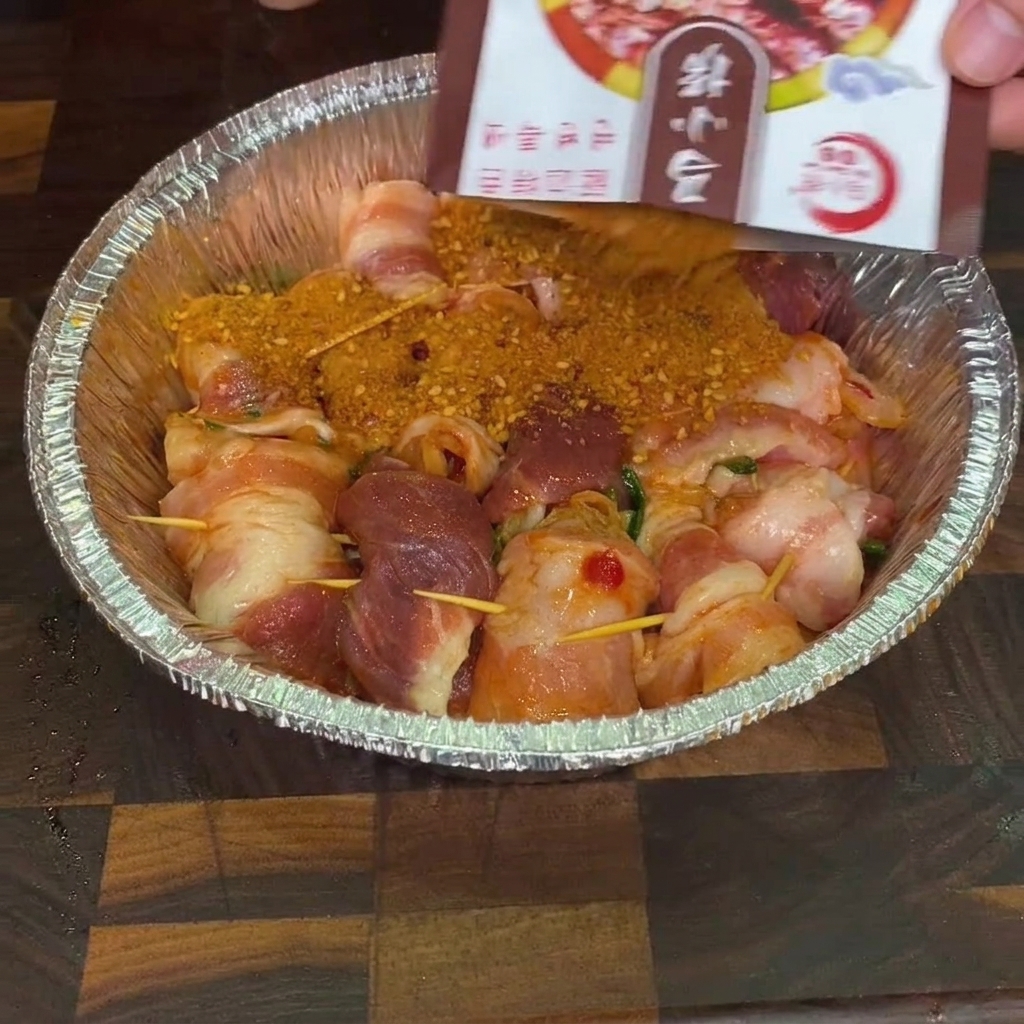Barbecue seasoning being sprinkled from a packet over raw pork rolls in an aluminum pan.