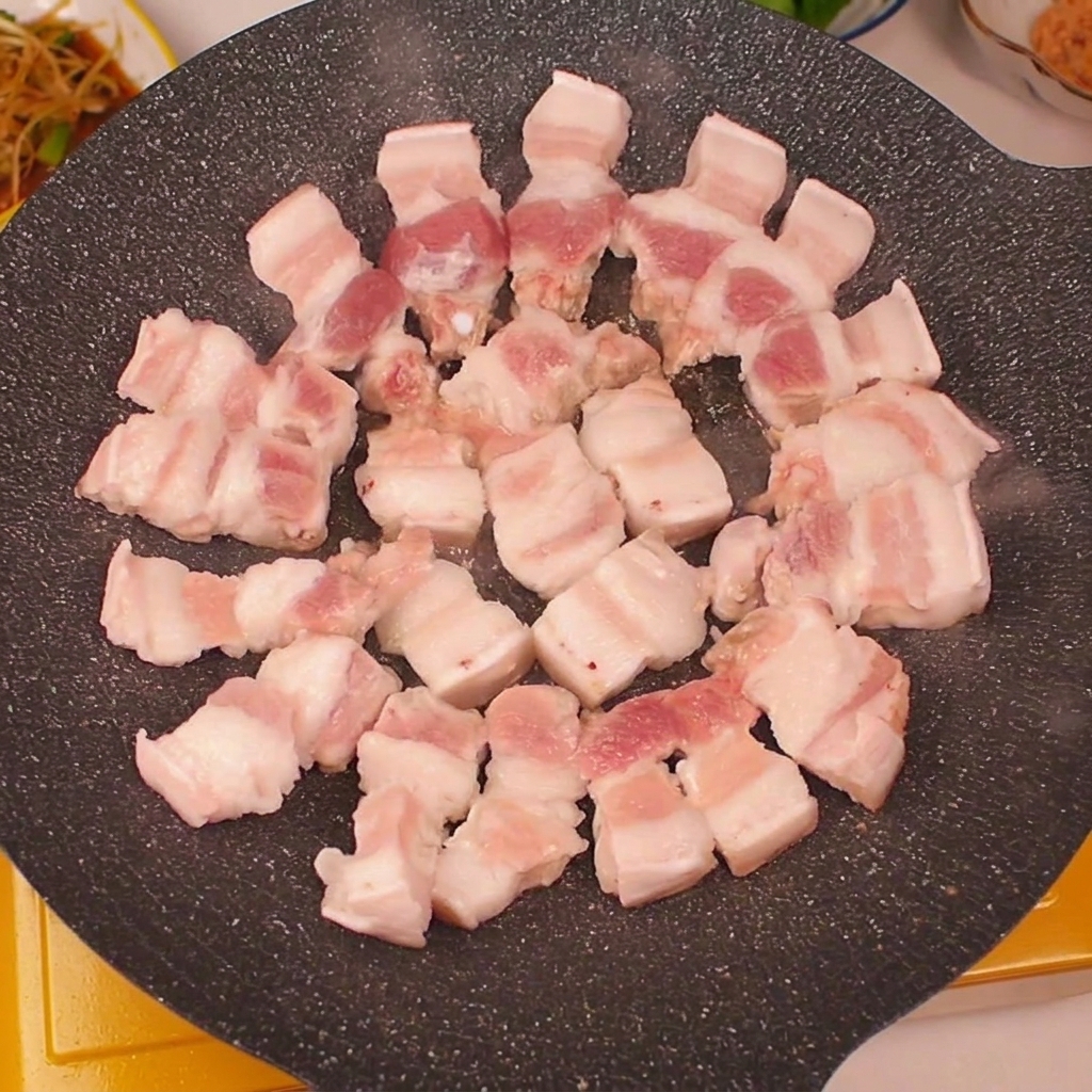 Fresh pork belly strips neatly laid out in a circular pattern on a dark, hot grilling pan.