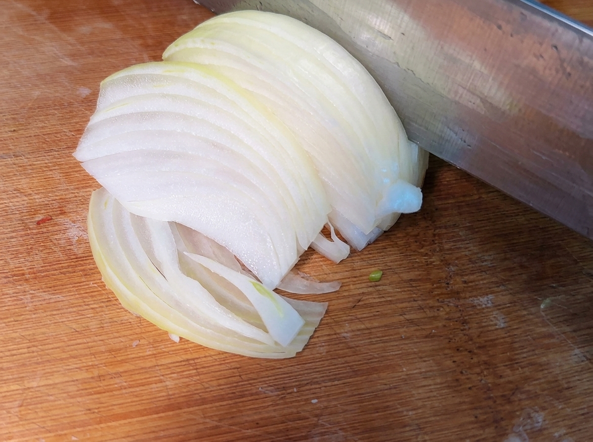 Freshly sliced thin onion strips piled on a wooden cutting board.